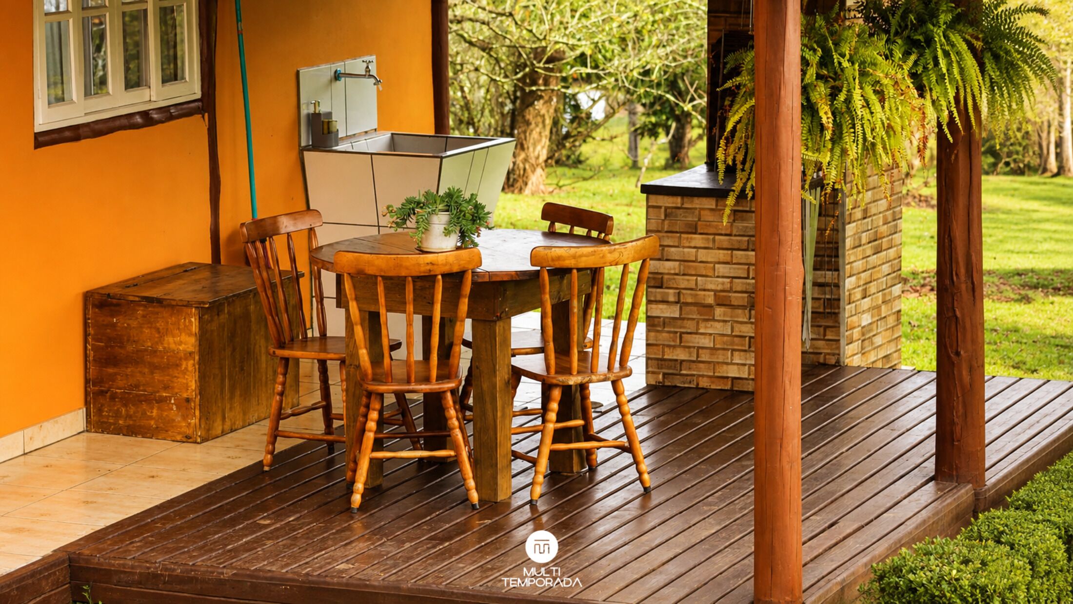 Una terraza de madera con una mesa y sillas, un muro de ladrillo y vistas al jardín.