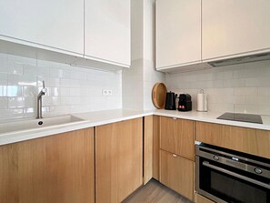 A modern kitchen with white cabinets, a stainless steel sink, and a built-in oven. - Viva Riviera Sunny Apartment with Balcony (Cannes)