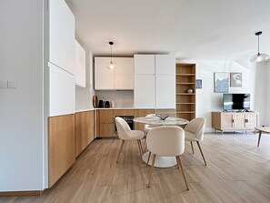 A modern kitchen with wooden cabinets, a dining table with chairs, and a built-in bookshelf. - Viva Riviera Sunny Apartment with Balcony (Cannes)