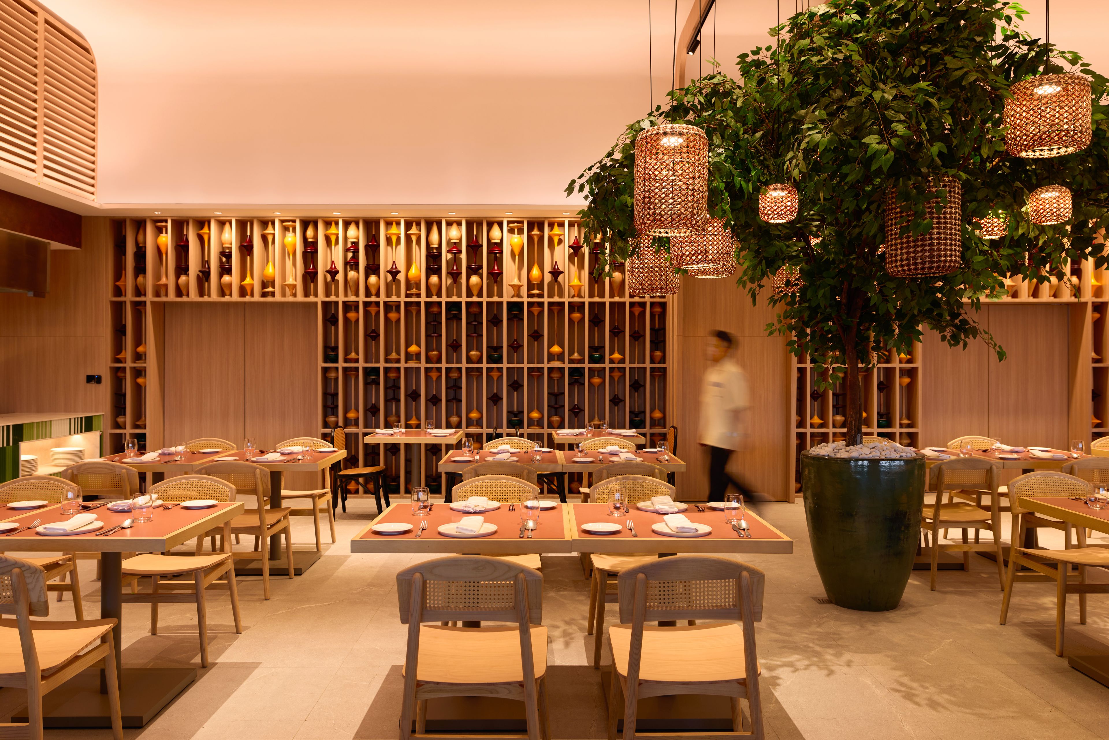 A restaurant interior with multiple dining tables, chairs, and hanging wicker lamps.