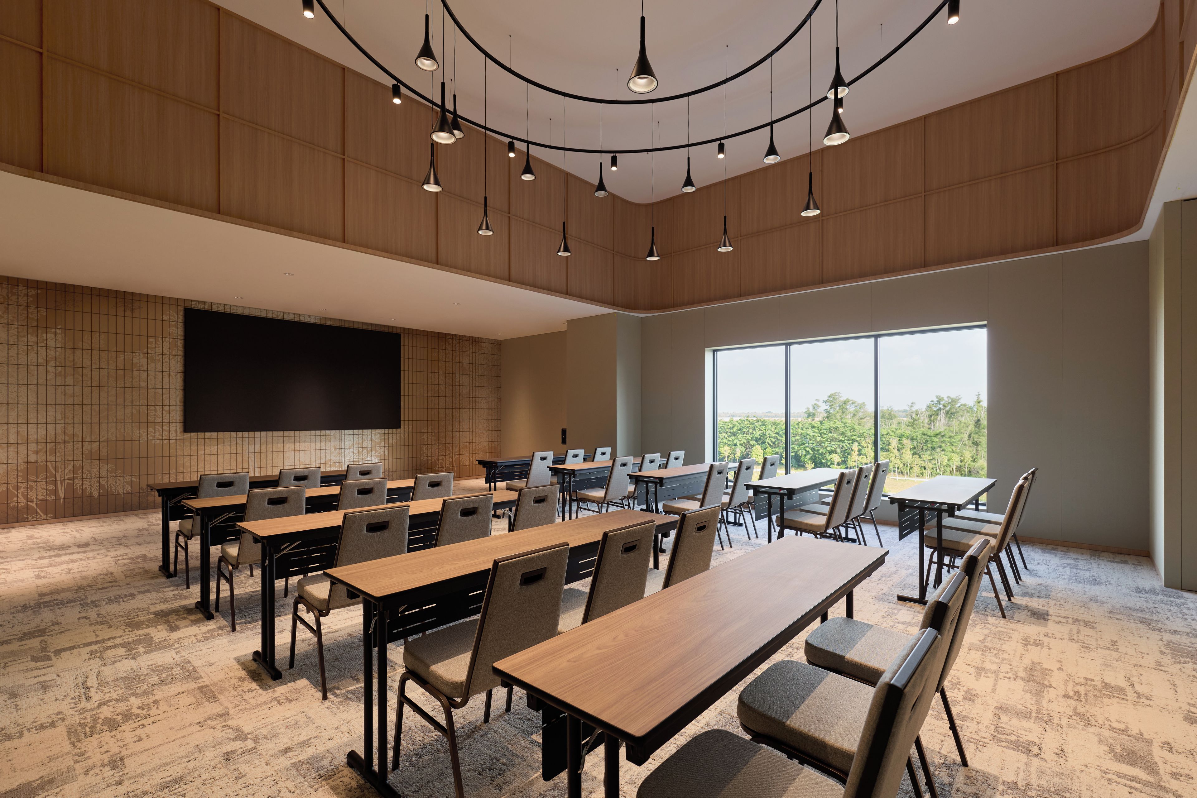 A conference room with multiple tables and chairs, a large screen, and a view of the outdoors through large windows.