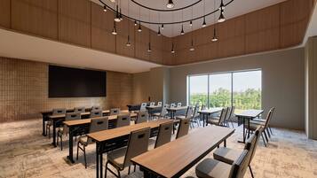 A conference room with multiple tables and chairs, a large screen, and a view of the outdoors through large windows.