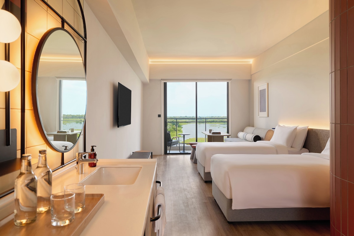 A hotel room with a large mirror, a bed, a desk, and a view of the outdoors.