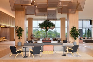 A spacious lobby with a seating area, large windows, and a view of greenery outside.