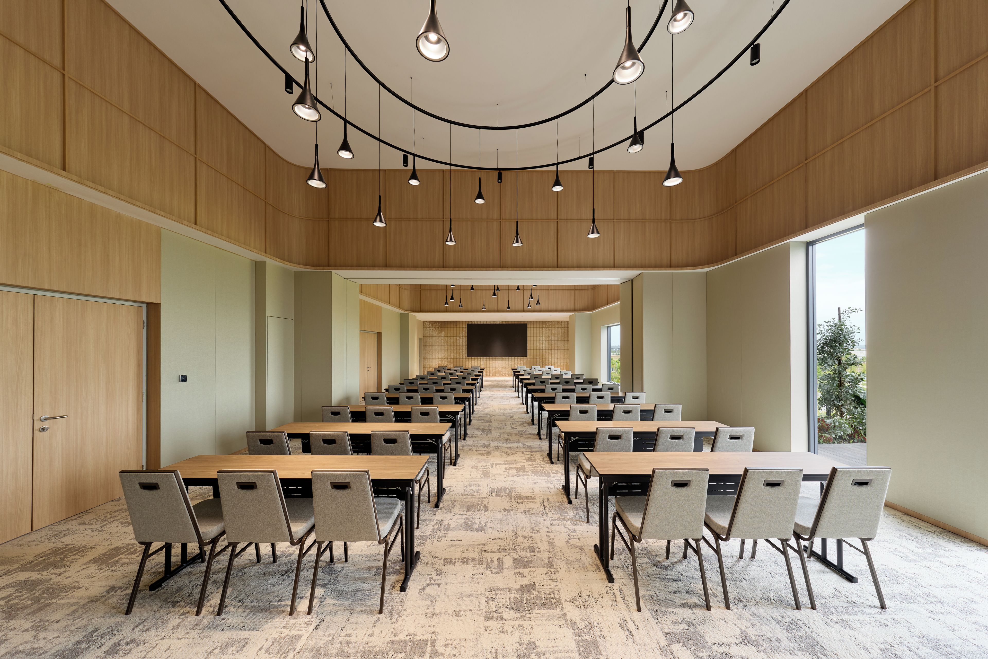 A conference room with multiple tables and chairs, wooden panel walls, and pendant lighting.