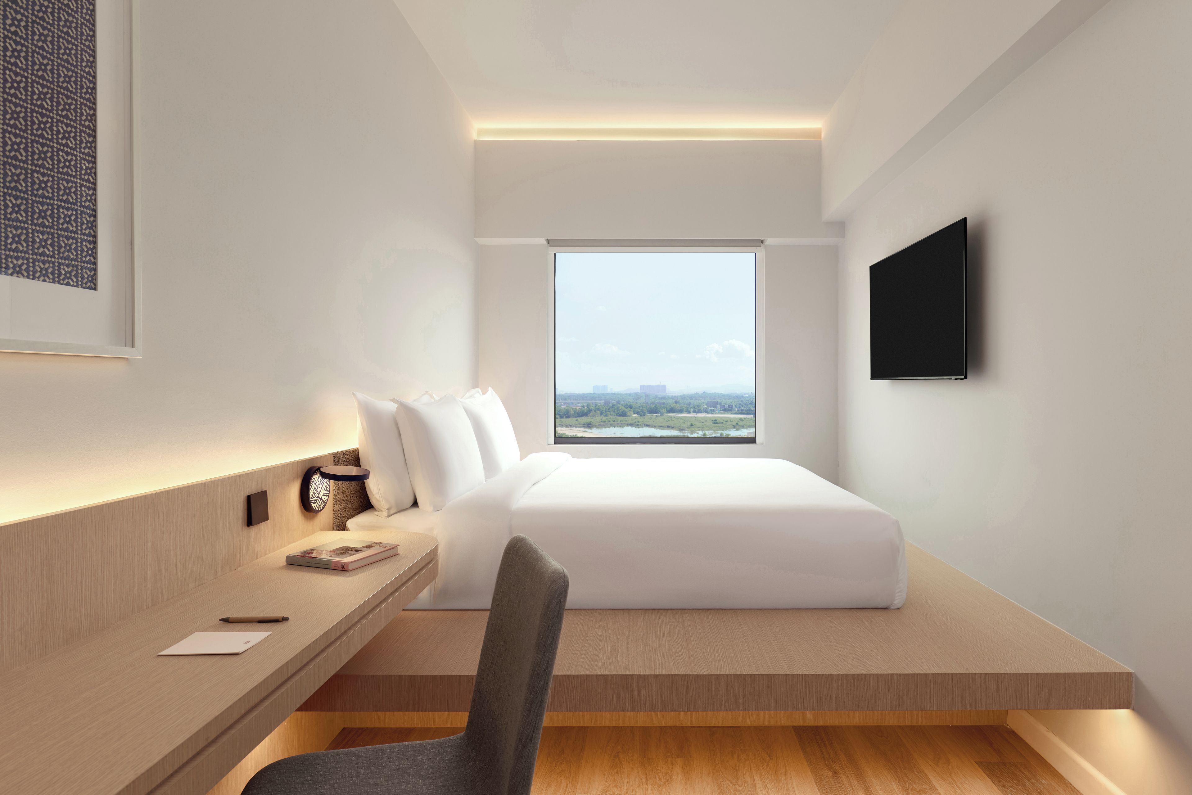 Ein modernes Hotelzimmer mit Bett, Schreibtisch, Stuhl, Fernseher und großem Fenster mit Blick auf die Stadt.
