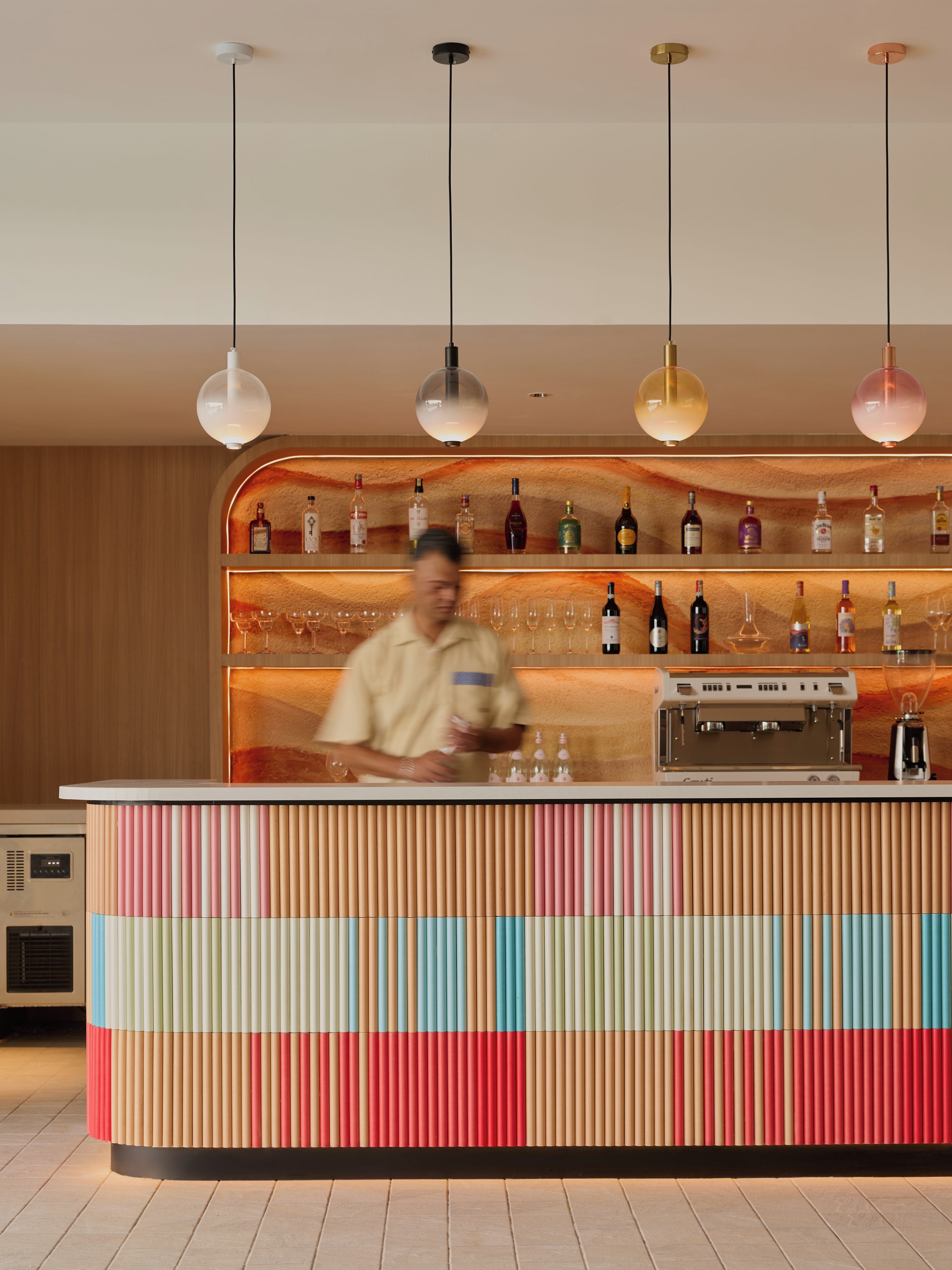 Una zona de bar con un cantinero, una variedad de botellas de licor y una máquina de café.