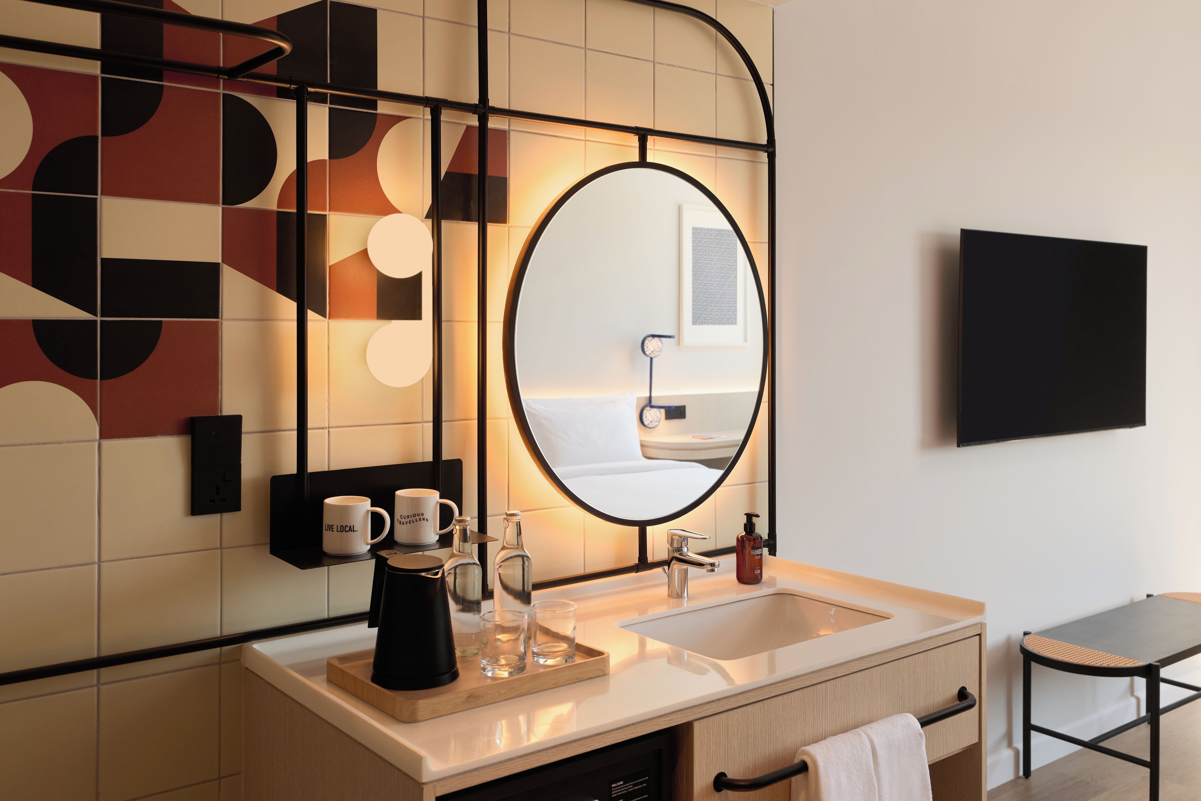 Un baño moderno con un espejo grande, un lavamanos y una cafetera.