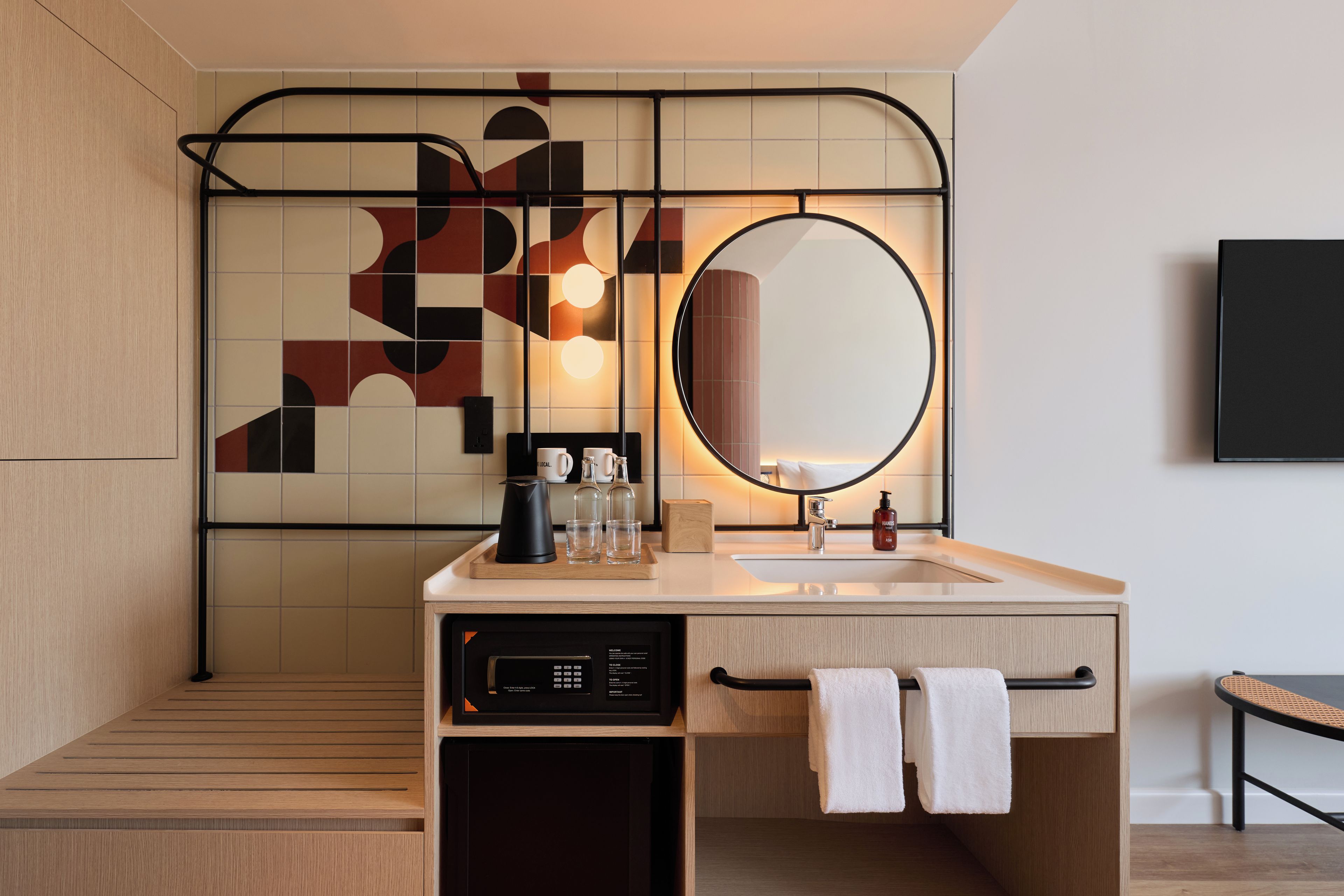 A modern bathroom with a wooden floor, a sink with a mirror, a coffee maker, and a towel rack.