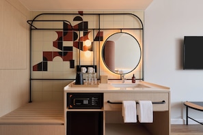 A modern bathroom with a wooden floor, a sink with a mirror, a coffee maker, and a towel rack.