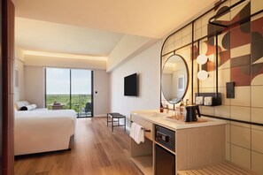 Habitación de hotel con cama, una mesita, una silla, baño con lavamanos, espejo y vista al exterior.