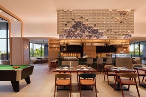 A modern dining area with a pool table, bar seating, and a kitchen area.