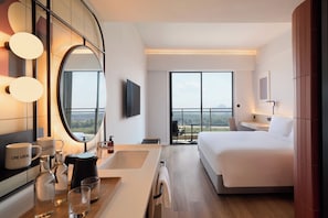 A modern hotel room with a large bed, a sitting area with a view, a bathroom with a mirror and sink, and a large window. - Asai Gamuda Cove (Banting)