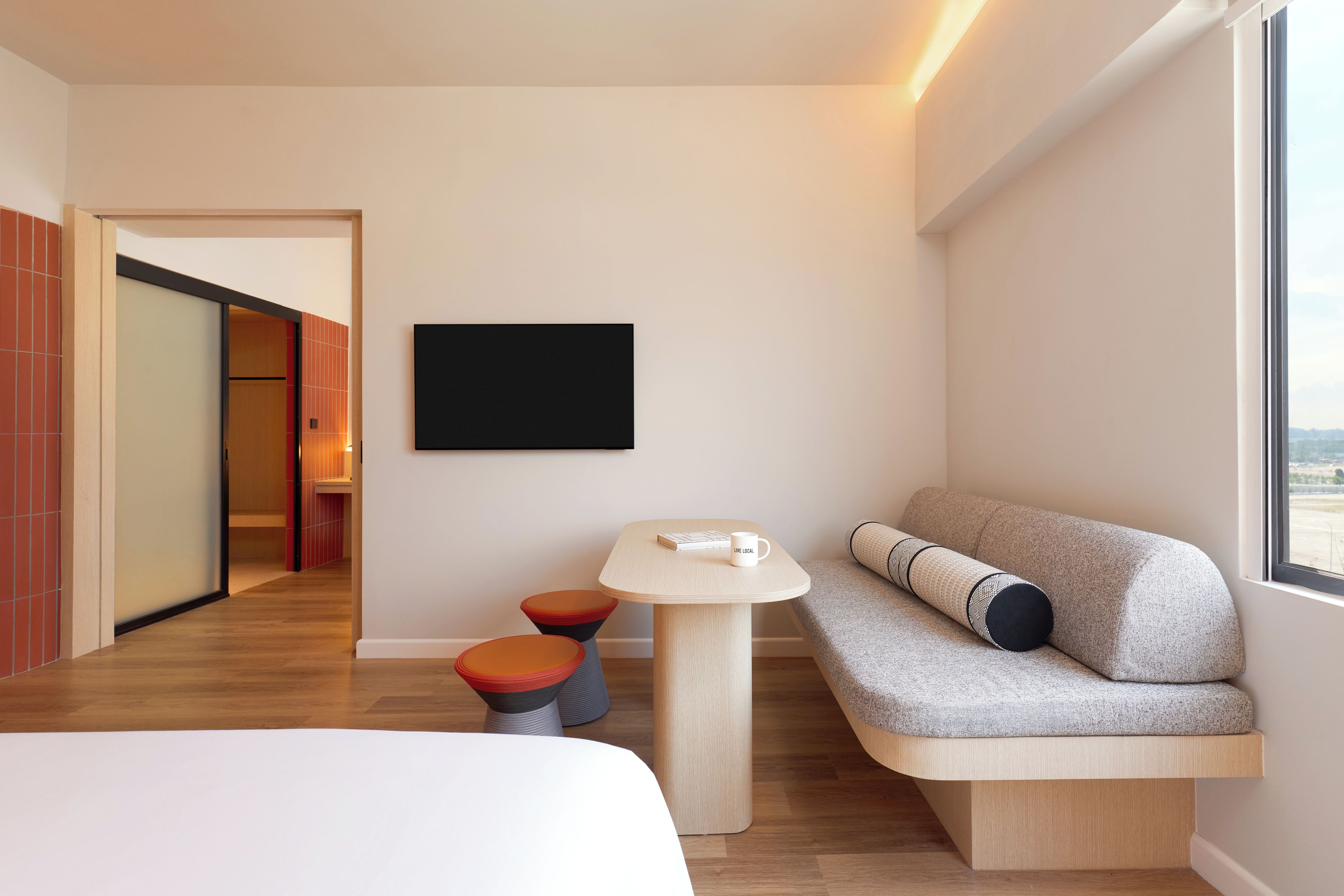 A modern hotel room with a sofa, a small table, and a TV on the wall.