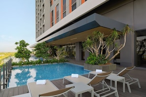 A modern outdoor pool area with lounge chairs and a view of a high-rise building. - Asai Gamuda Cove (Banting)