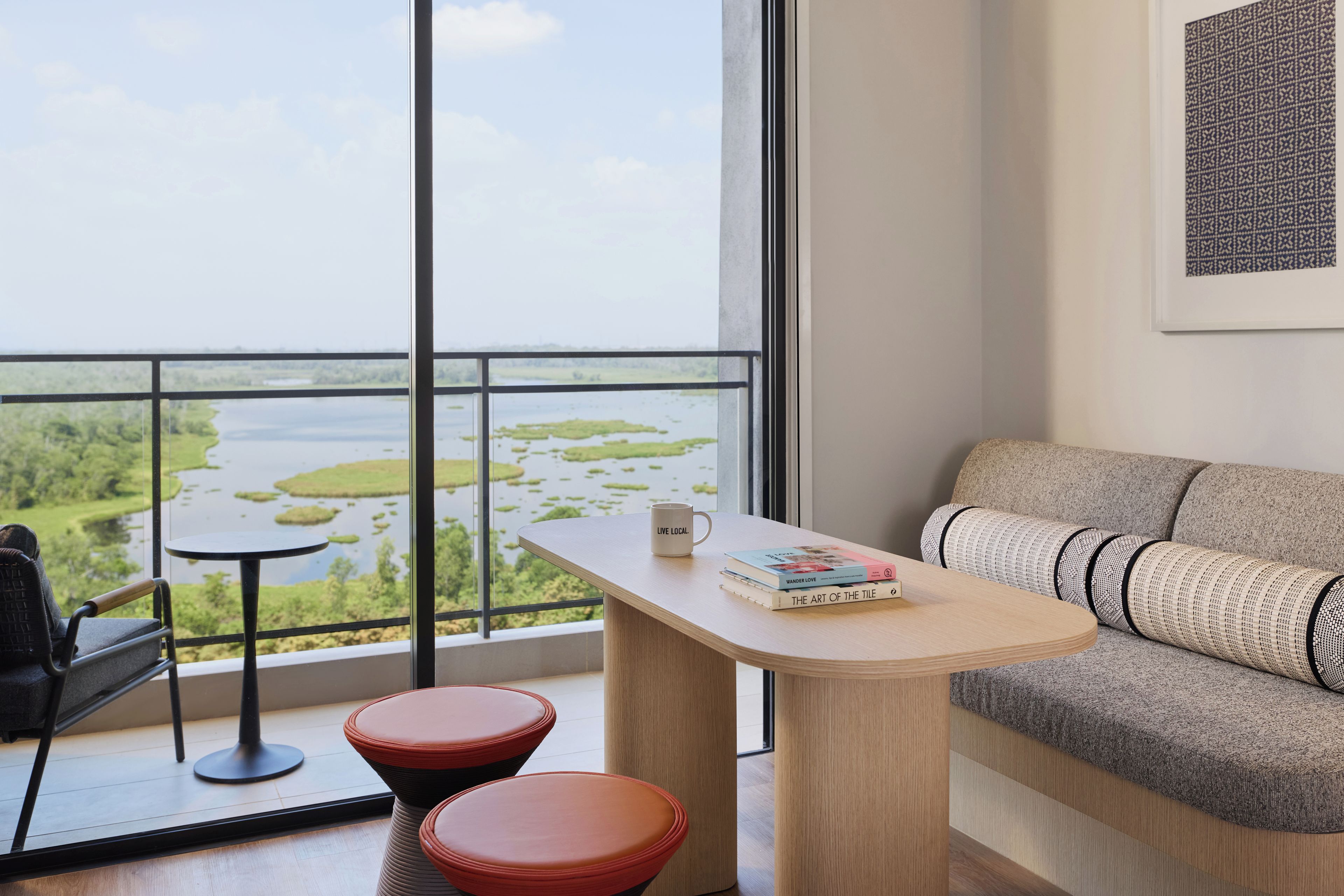 Una habitación moderna con balcón, un sofá, una mesa y dos taburetes rojos.