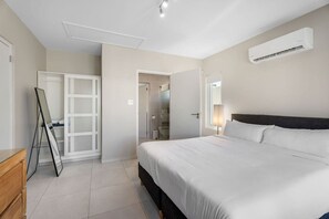 Una habitación de hotel con una cama grande, un armario, un espejo y un aire acondicionado.