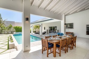 A covered outdoor dining area with a pool, wooden furniture, and a view of the pool and greenery. - NEW 3BR Luxe Villa in Esmeralda by Signature Stays (Noord)