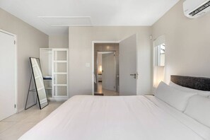 Ein modernes Hotelzimmer mit einem großen Bett, einem begehbaren Kleiderschrank und einem durch eine offene Tür einsehbaren Badezimmer.