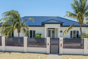 Ein modernes, zweistöckiges Haus mit blau gefliestem Dach, einem verschlossenen Eingang und Palmen.