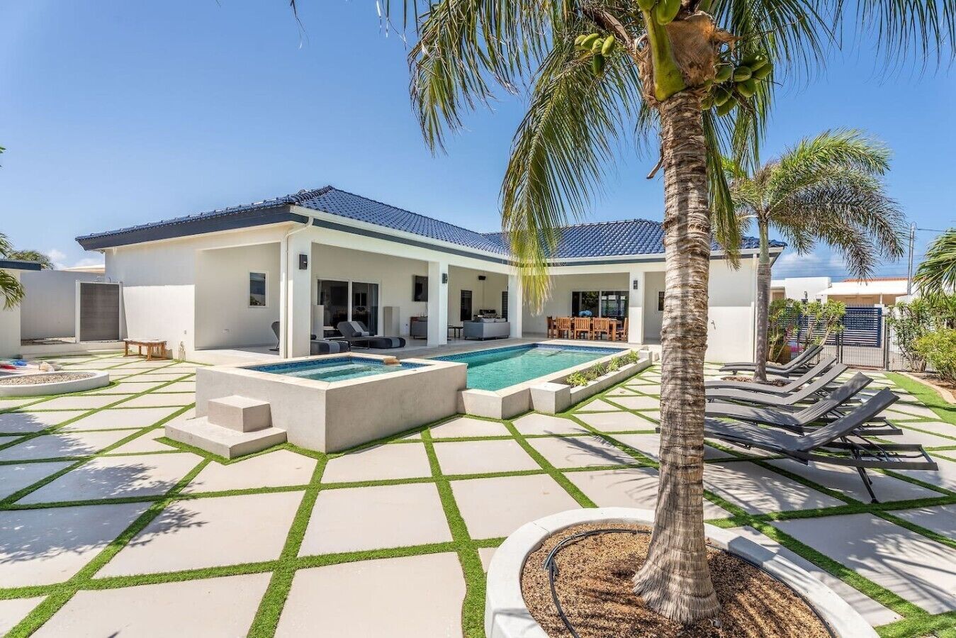 Una casa moderna con piscina, mobiliario exterior y palmeras.
