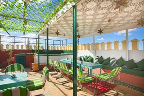 An outdoor patio with green-striped chairs and tables, a patterned ceiling, and a view of the cityscape. - Riad Dar Lefna (Marrakech)