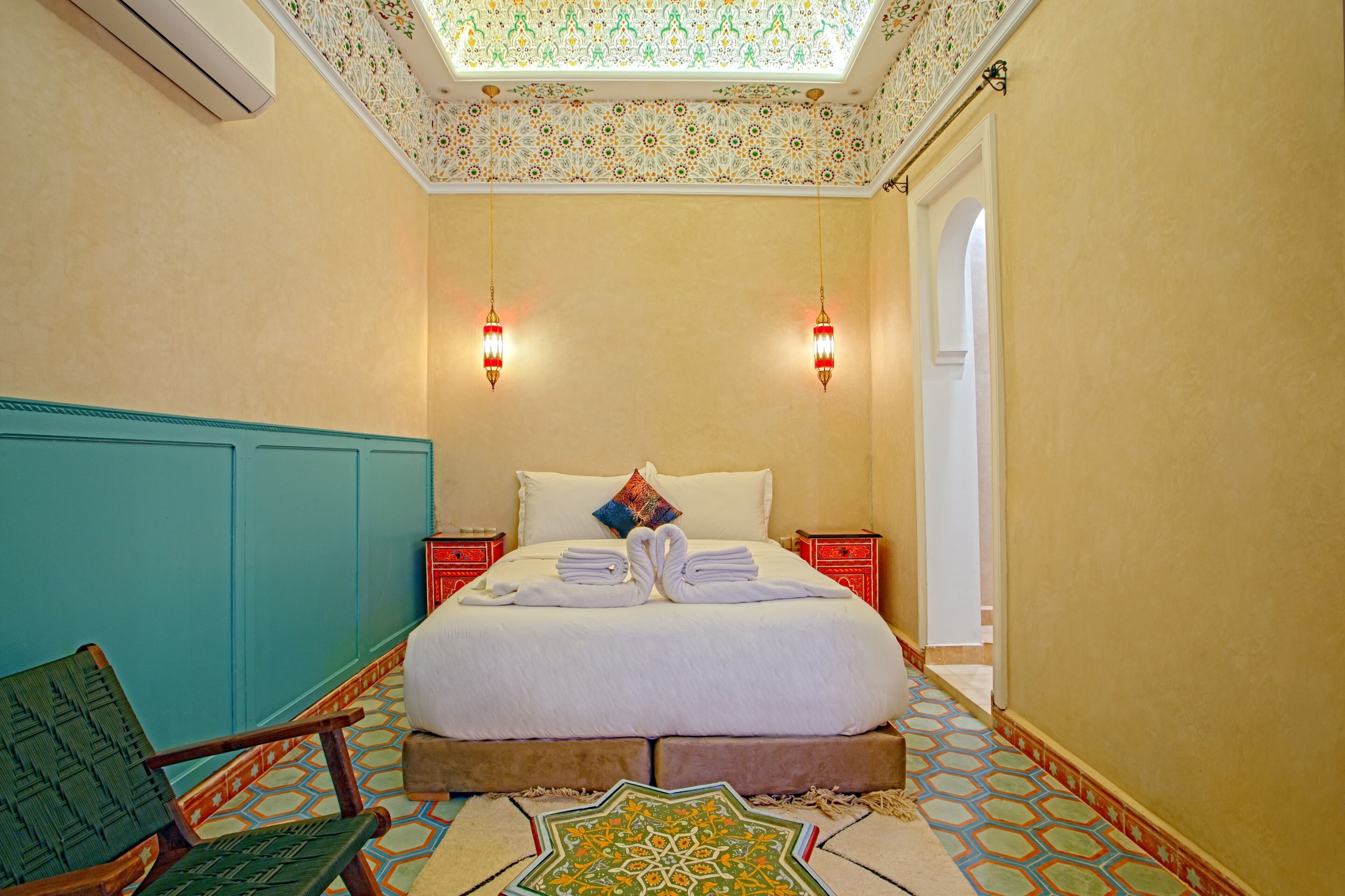 Una habitación de hotel con una cama, dos mesitas de noche, una silla, piso estampado y techo decorativo.