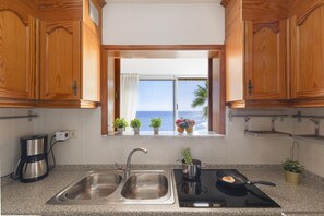 A kitchen with wooden cabinets, a double sink, a stove, and a window with a view of the sea. - Nueva Suecia 421 by VillaGranCanaria (Maspalomas)