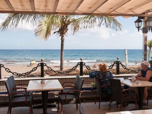 An outdoor seating area with tables and chairs overlooking a beach. - Nueva Suecia 421 by VillaGranCanaria (Maspalomas)