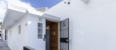 A white building with a wooden door, a black metal gate, and a small window.