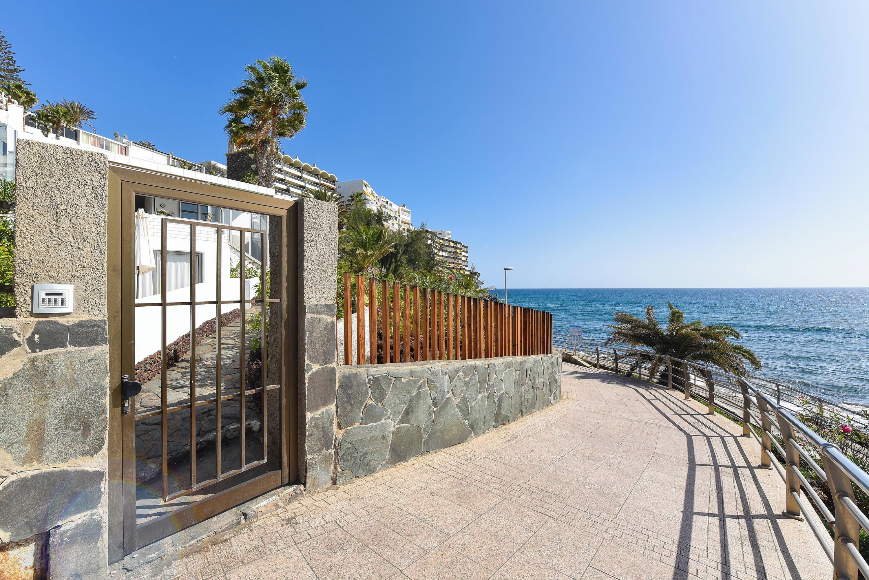 Une propriété située sur la côte, dotée d’une façade en pierre, d’une porte d’entrée en verre et d’un chemin pavé menant à la mer.