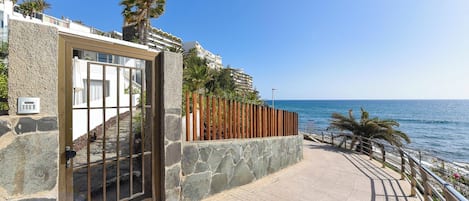 A coastal property with a stone facade, a glass door entrance, and a paved walkway leading to the sea.