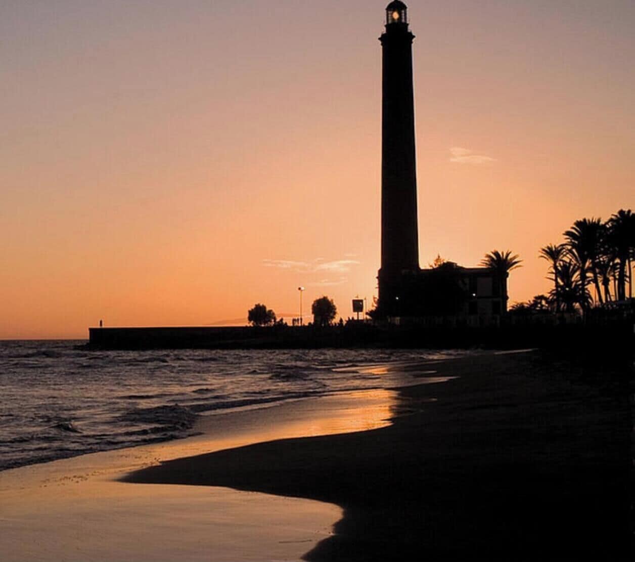 A lighthouse at sunset with a beach in the foreground.