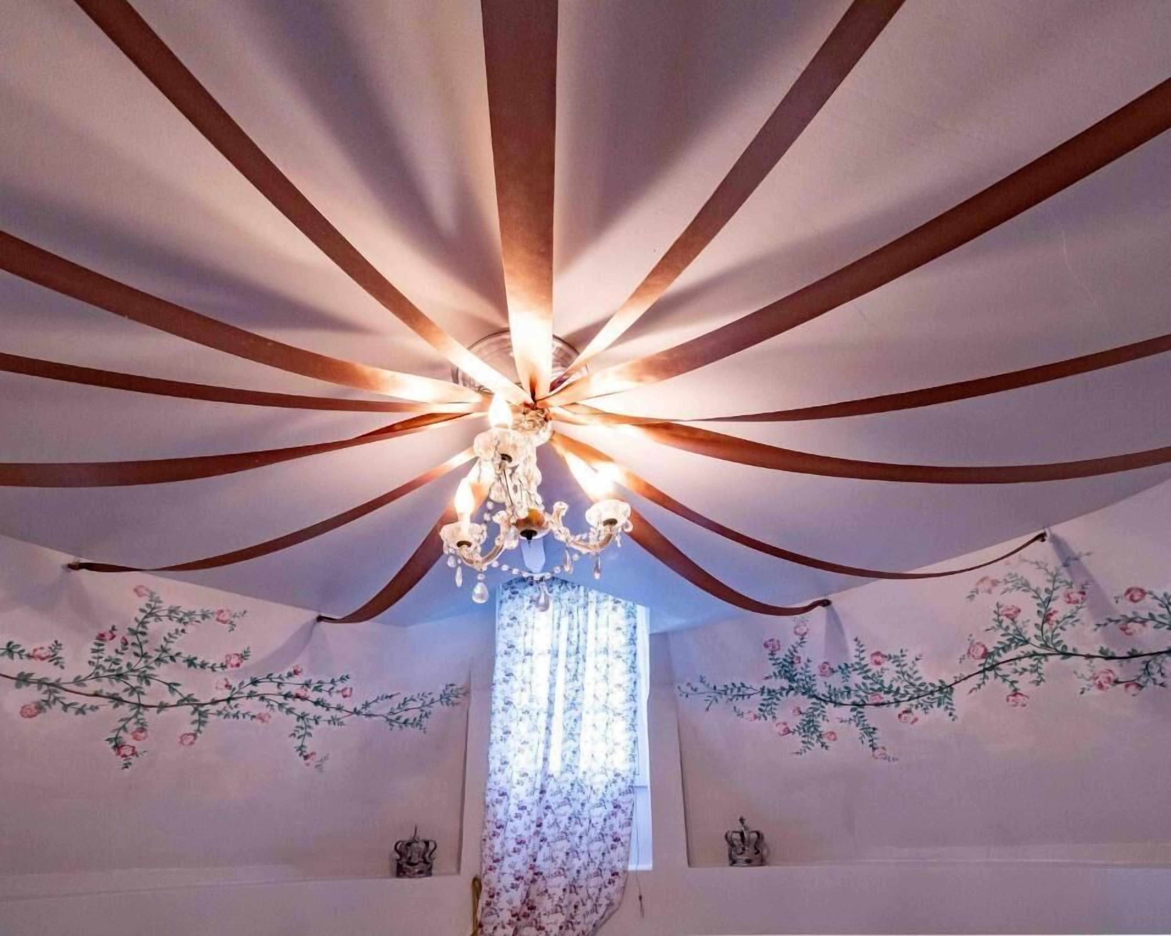 Een kamer met een kroonluchter, bloemendecoratie aan de muur en een raam met dunne gordijnen.