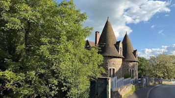 A stone building with multiple conical roofs, surrounded by trees and a metal fence.