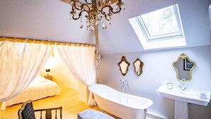A bedroom with a canopy bed, a bathtub, a vanity with a mirror, and a chandelier.