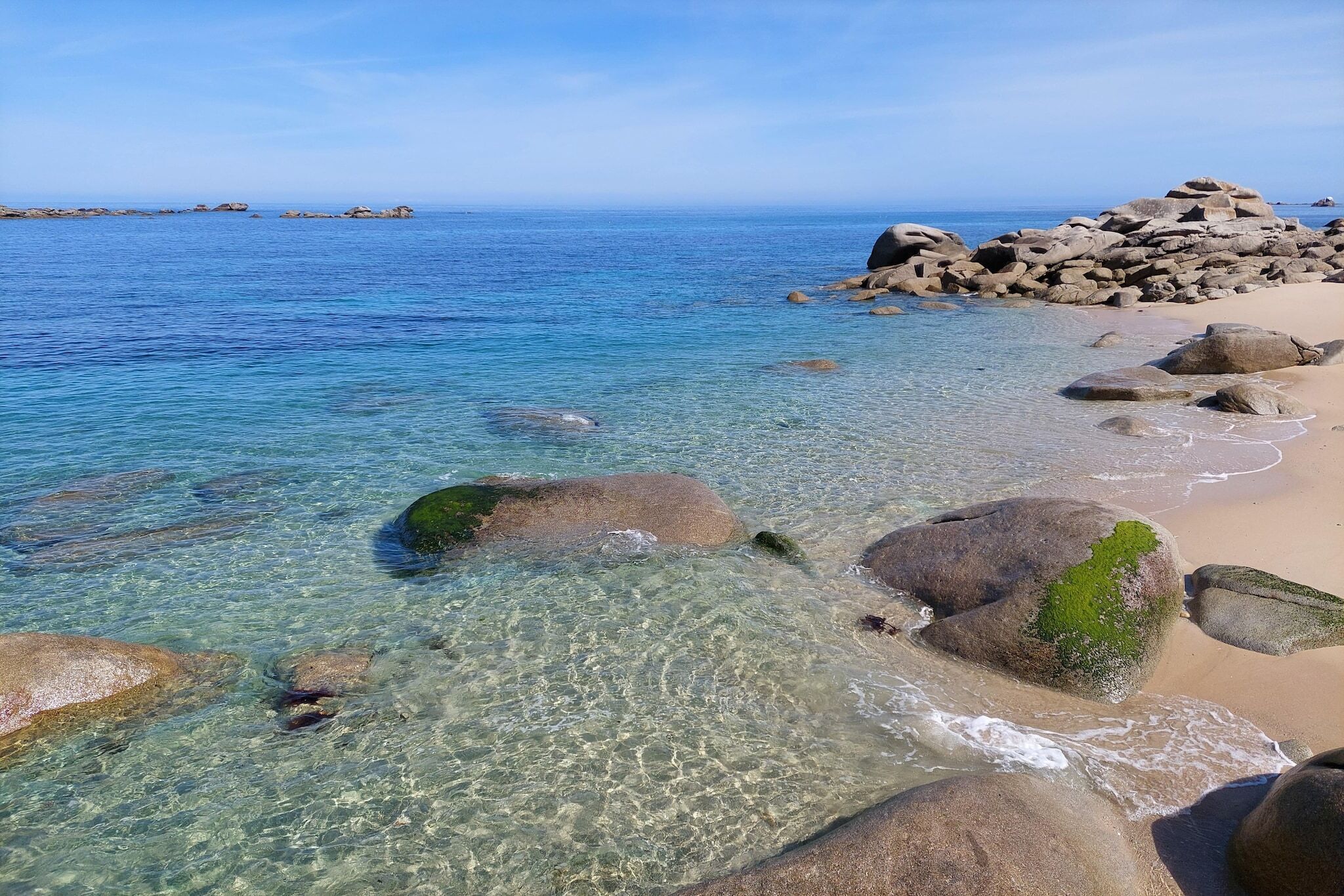 A beach with clear water, rocks, and a distant shoreline.