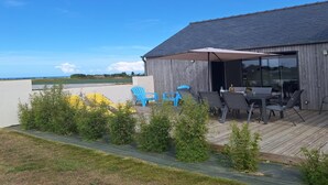 A covered outdoor seating area with tables and chairs, a wooden deck, and a view of the sea. - House in Brittany with sea view for 2 people. (Cléder)