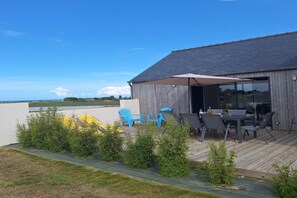 Ein überdachter Außenbereich mit Tischen und Stühlen, einer Holzterrasse und Blick auf das Meer.
