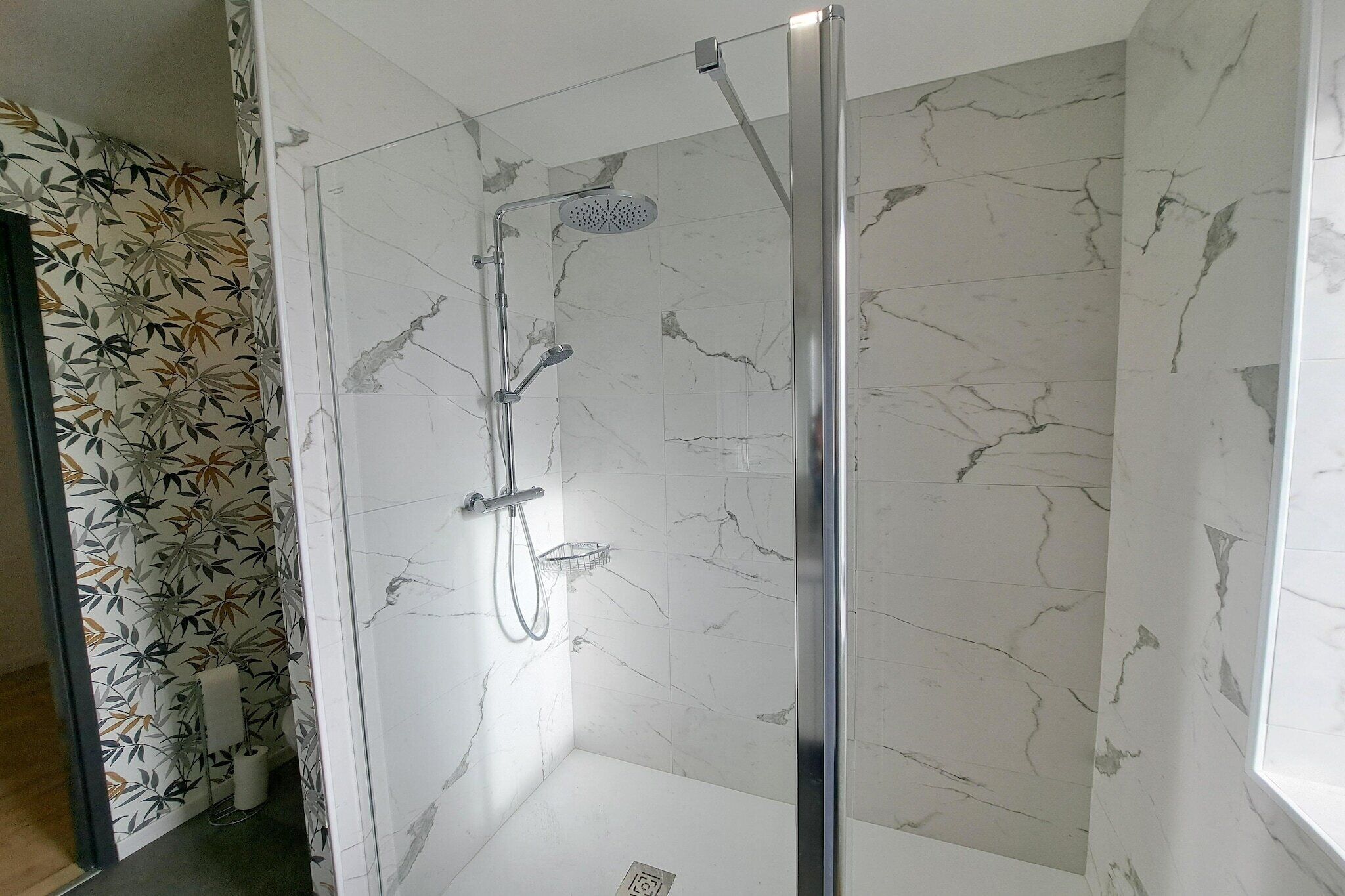 A glass-enclosed shower with a handheld showerhead and a wall-mounted faucet.