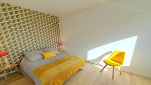 A bedroom with a bed, a yellow chair, a red lamp, and a geometric wall pattern. - House in Brittany with sea view for 2 people. (Cléder)
