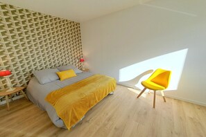 Ein Schlafzimmer mit einem Bett, einem gelben Sessel, einer roten Lampe und einem geometrischen Wandmuster.