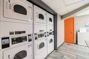 Een wasserette met meerdere wasmachines, genummerd van 1 tot 6, en een bedieningspaneel met digitale beeldschermen.