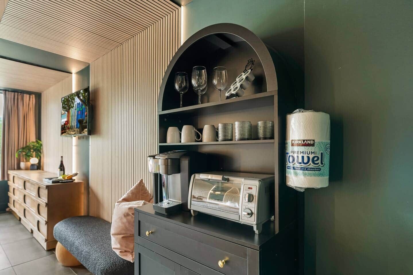Ein modernes Wohnzimmer mit Kaffeemaschine, Bücherregal mit Dekoration und einem an der Wand befestigten Toilettenpapierhalter.