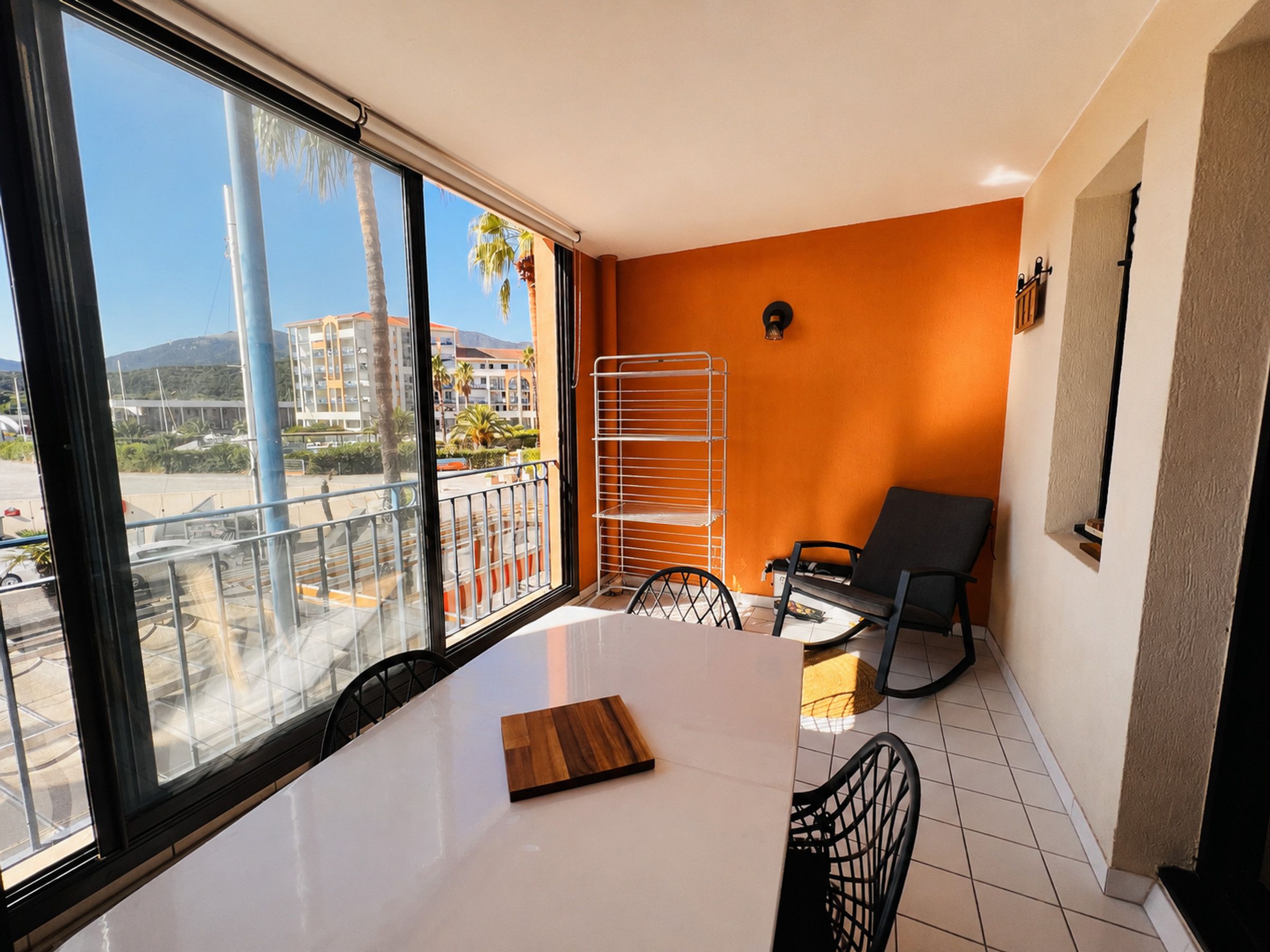 Una habitación con un ventanal grande, una mesa con una tabla de madera, una silla y un perchero metálico.