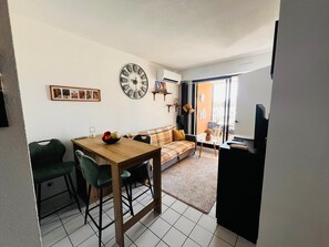 A living room with a dining area, a sofa, a coffee table, a clock, and a view through a glass door. - Apartment for 4 guests in Argelès-sur-Mer (Argelès-sur-Mer)