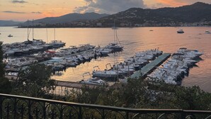 Un puerto deportivo con barcos amarrados, montañas al fondo y un cielo al atardecer.