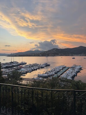 A marina with boats docked, a mountainous backdrop, and a sunset sky.