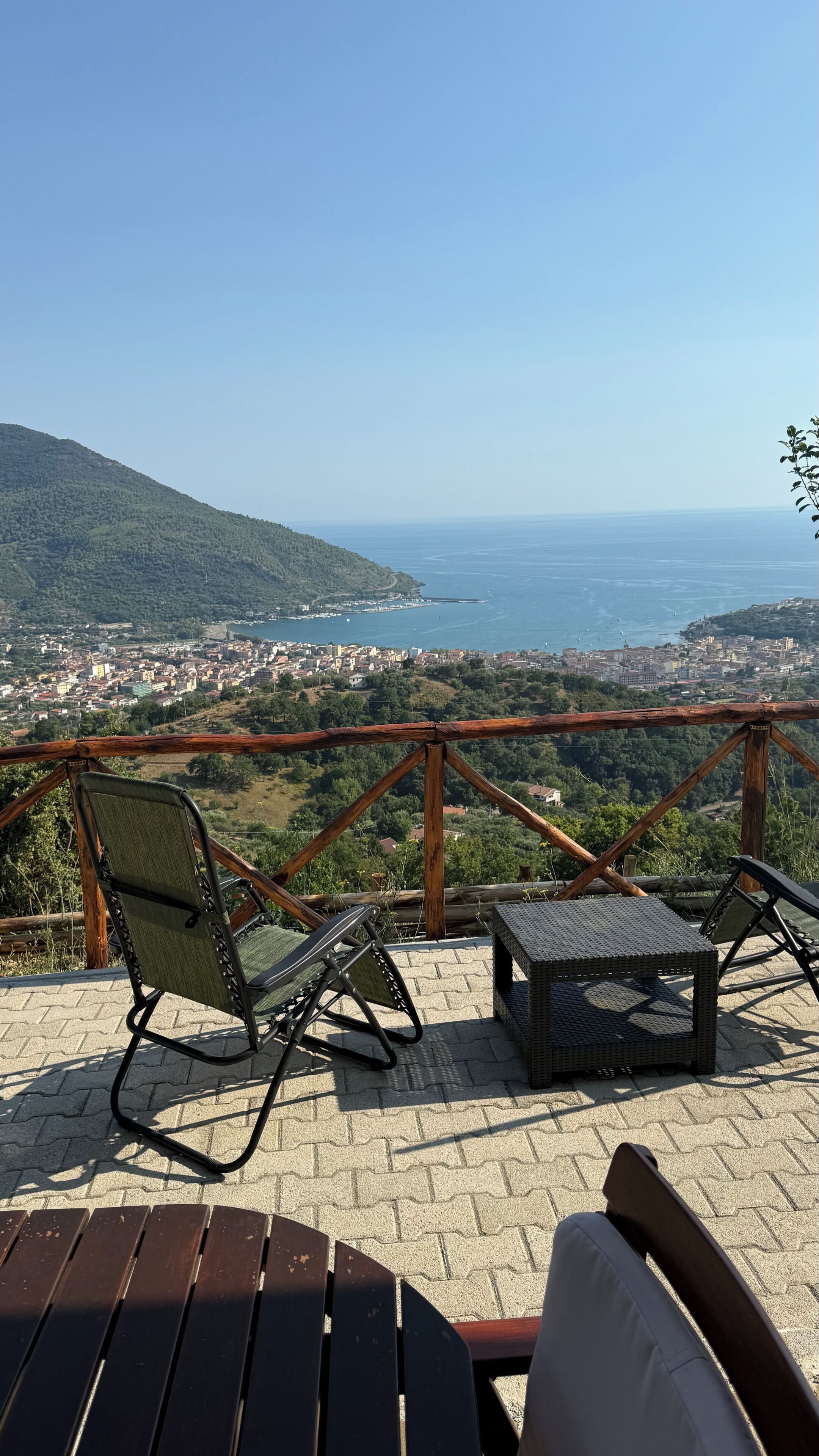 Eine Terrasse mit zwei Stühlen und einem kleinen Tisch mit Blick auf eine Küstenstadt und das Meer.