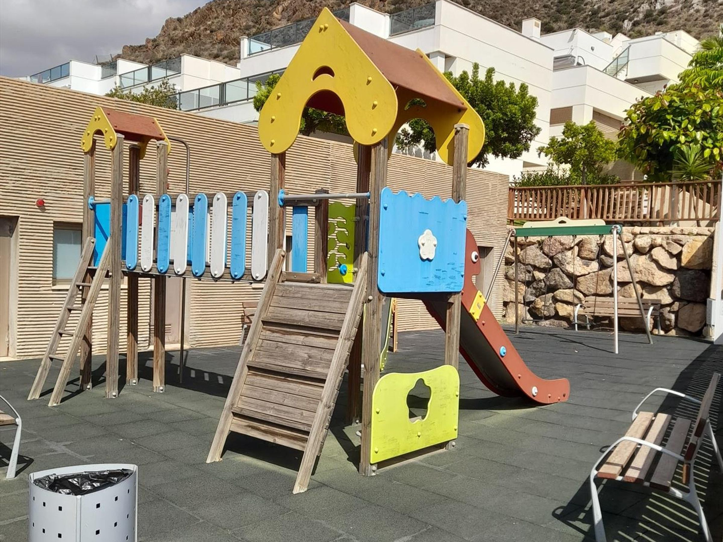 A playground with a wooden slide, climbing structures, and a blue climbing wall.
